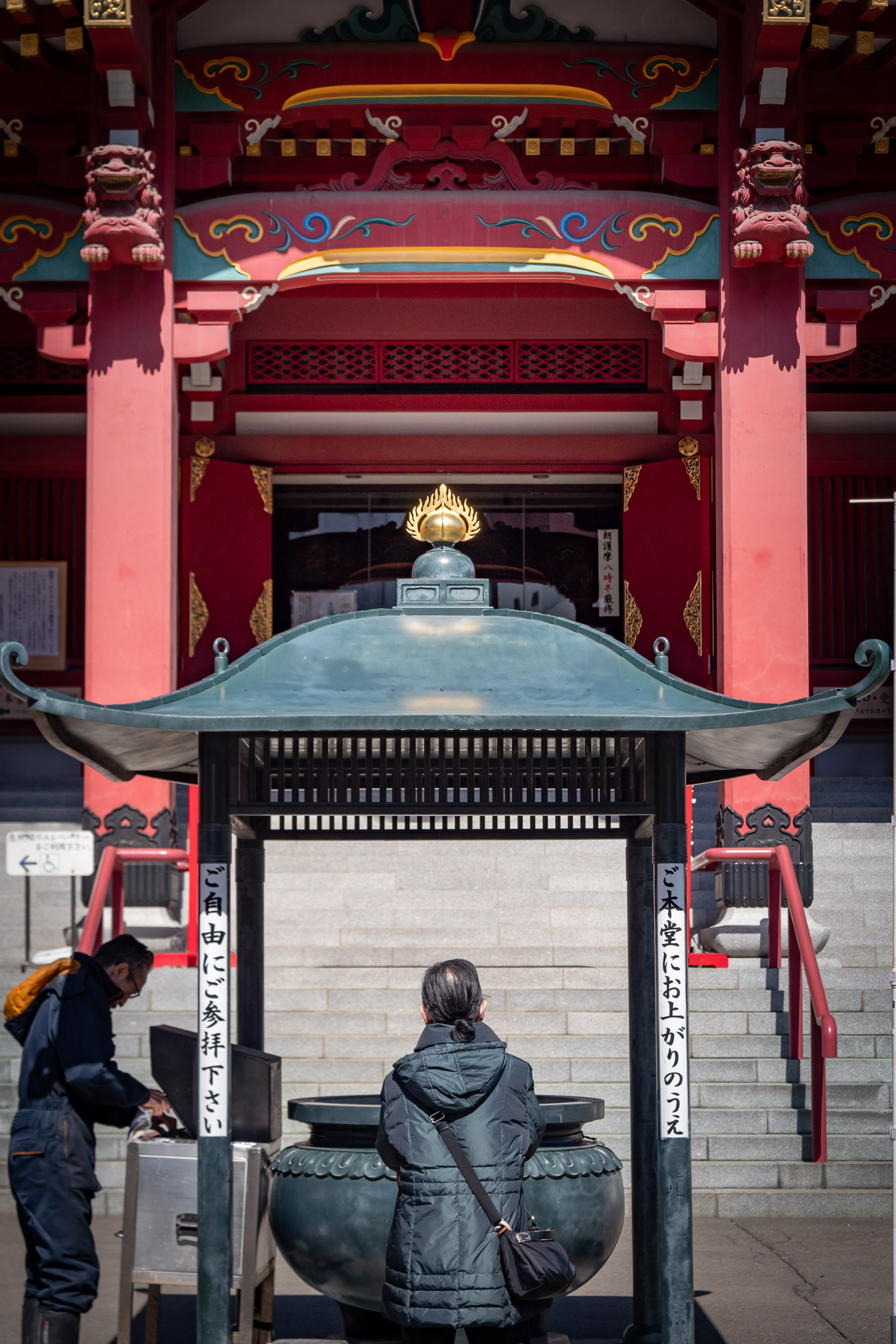 青空の下、ビルの谷間の成田山札幌別院新栄寺で祈祷する参拝客　DMC-GX8 + LEICA DG 12-60mm