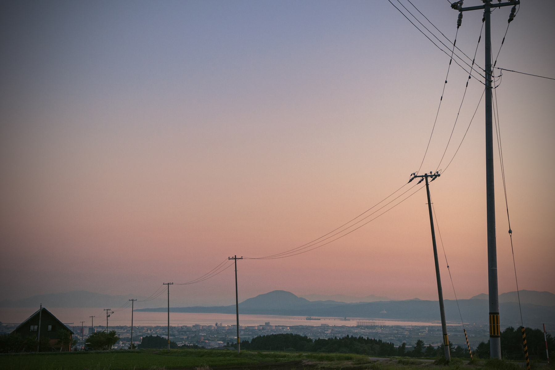 函館市亀田中野町「石川の丘」から眺める宵闇迫る函館湾　茜色の空に連なる電信柱のシルエットと海へ連なる一本の道