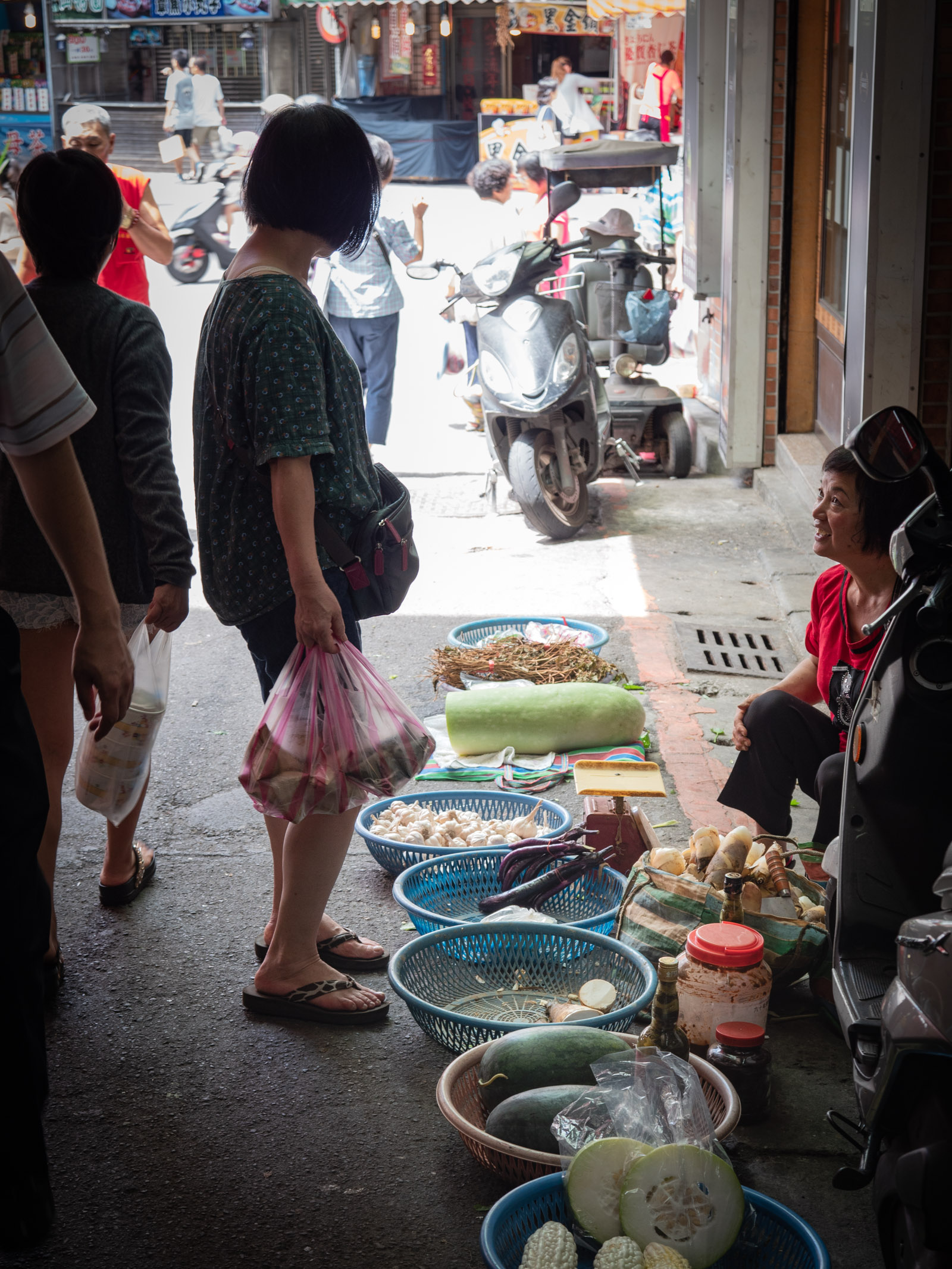 買い物客とおしゃべりに興ずる野菜の路上販売の女性